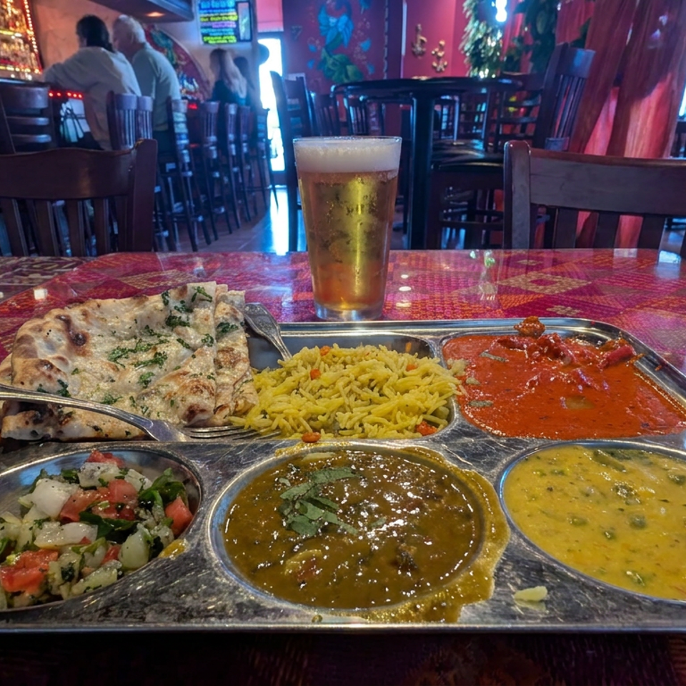 Indian thali with naan, rice, curries, lentils, and salad on a colorful restaurant table beside beer and water.