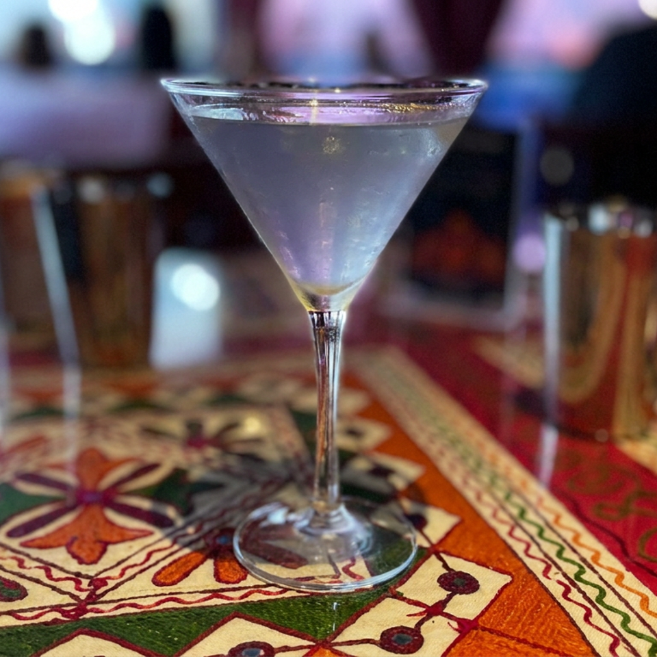 Frosted cocktail in a martini glass on a colorful patterned tablecloth inside a softly lit restaurant.