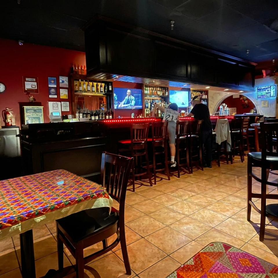 Colorful restaurant interior with red walls, a stocked bar, televisions, high tables, and patterned tablecloths.